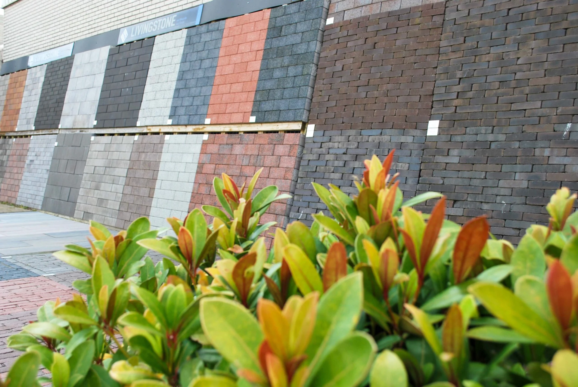 Een buitendisplay met verschillende soorten dakshingles in diverse kleuren en gebakken klinkers, geschikt voor daken, opritten en tuinbestrating.